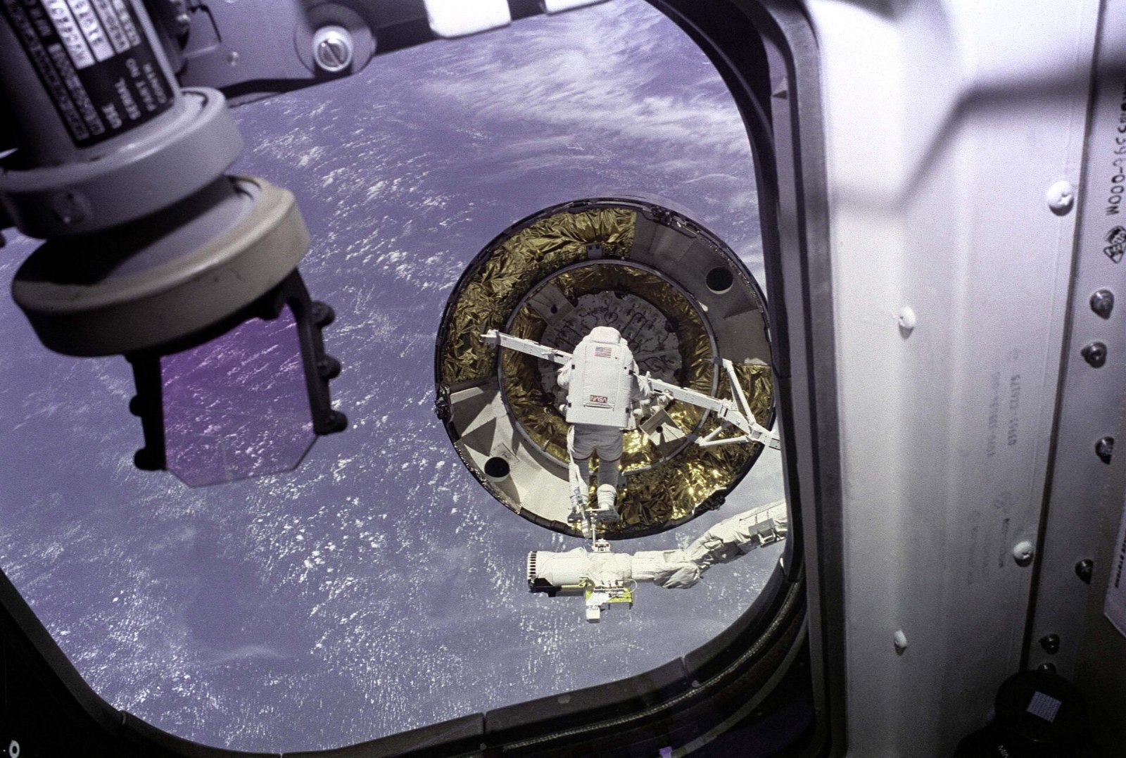 An astronaut on the Shuttle robotic arm reaching toward the Intelsat VI satellite with a capture bar