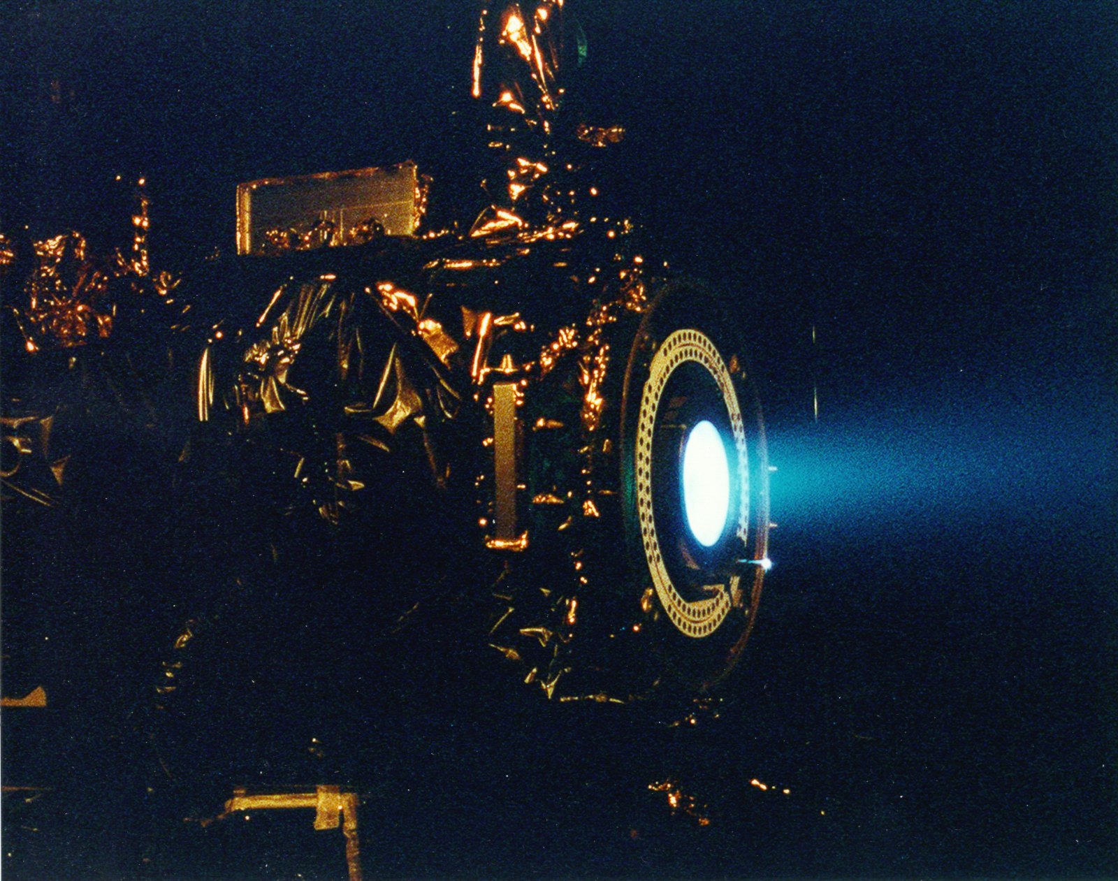 A xenon ion engine emitting a faint blue plume inside a vacuum chamber