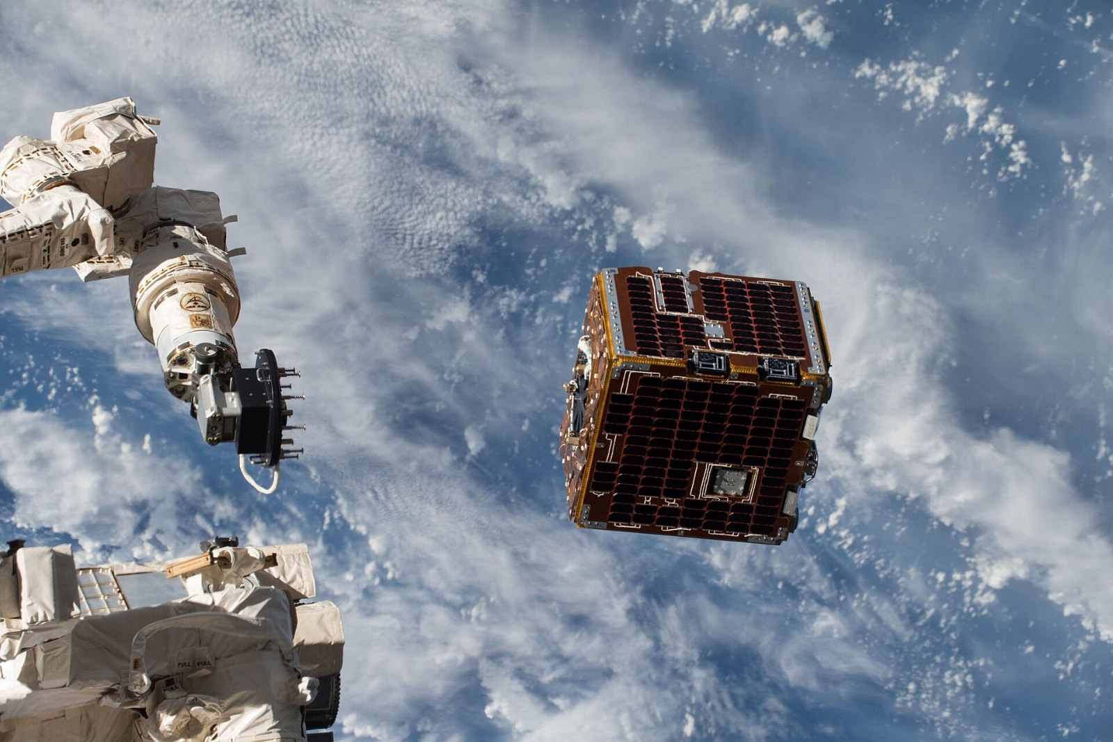 The RemoveDEBRIS satellite drifting away from the International Space Station above Earth