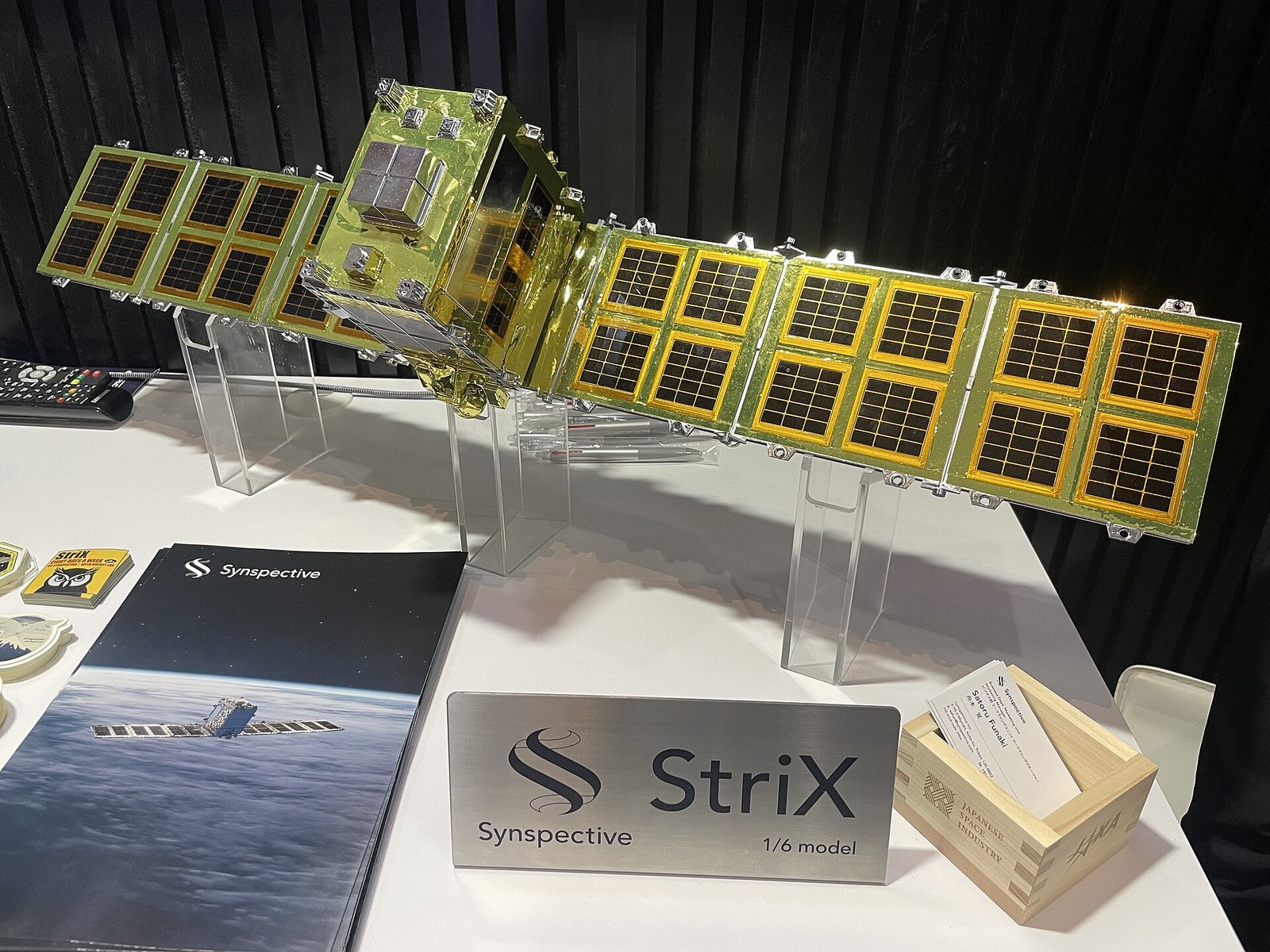 A scale model of a StriX radar satellite with a long flat antenna panel and a boxy body, on a display stand